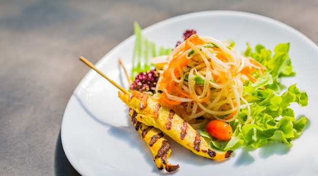 Famous Thai papaya salad or " Somtum" with Chicken satay on side.