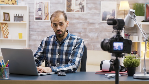 Famous young vlogger typing on laptop while talking with his subscribers on a podcast. Creative content creator.