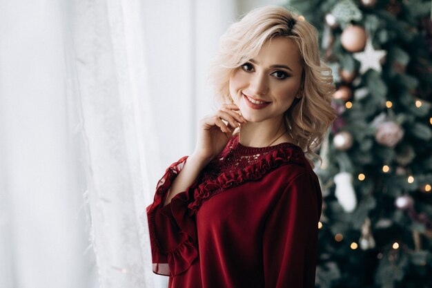 Fancy blonde woman dressed in red clothes stands in a room with Christmas decor