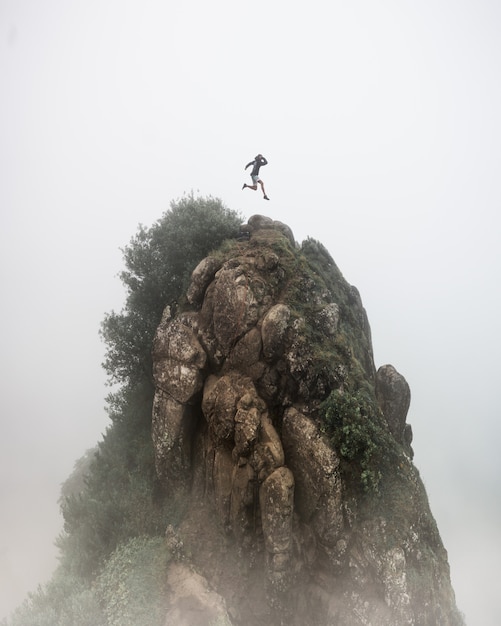 Fantasy concept - a person jumping over a high rocky cliff with a blurred foggy white background