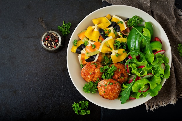 Farfalle pasta durum wheat with baked meatballs of chicken fillet  in tomato sauce and salad in bowl.