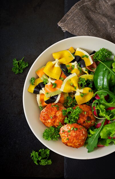 Farfalle pasta durum wheat with baked meatballs of chicken fillet in tomato sauce and salad in bowl.