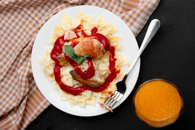 Farfalle with chicken leg and fork with orange juice on black surface