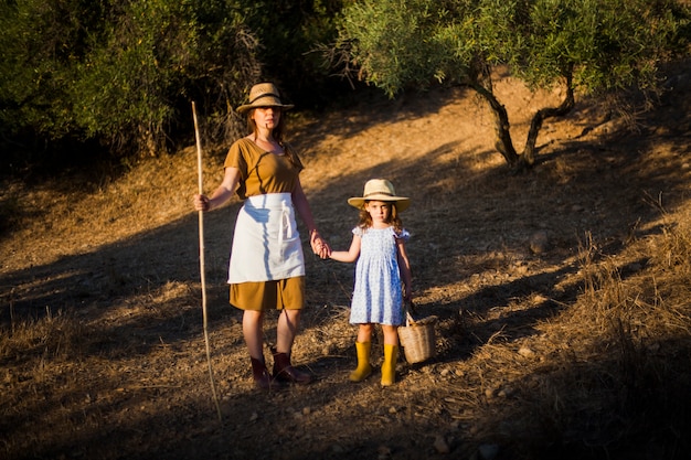 Free photo farmer woman holding her daughter's hand standing in the field