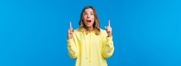 Fascinated and amused young blond girl drop jaw and staring speechless pointing fingers up at someth