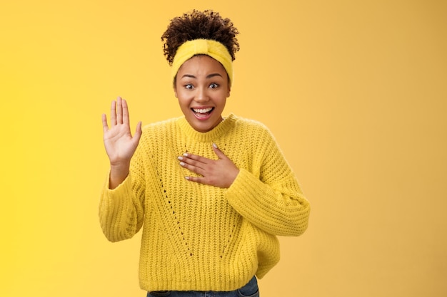 Affascinante divertito giovane affascinante sincera ragazza afro-americana fascia maglione stampa mano petto sollevare palmo giurando promettendo di fare del suo meglio in piedi eccitato sorridendo felicemente, in posa sfondo giallo.