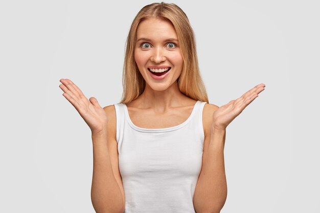 Fascinated beautiful cheerful woman cannot hold happiness inside, applauds and smiles positively, being excited by something, dressed casually, isolated over white wall. Body language concept