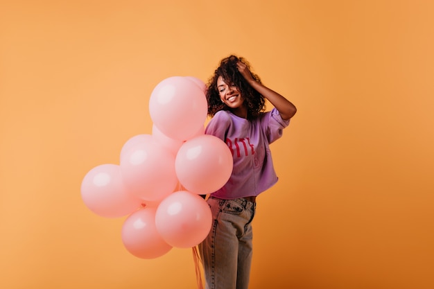 Free photo fascinating brunette girl with pink balloons posing with pleasure. adorable black lady chilling in her birthday.