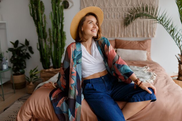 Fascinating brunette woman in straw hat chilling at home in cozy boho interior