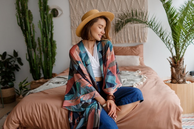 Fascinating brunette woman in straw hat chilling at home in cozy boho interior