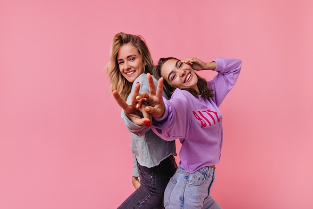 Fascinating emotional girls laughing and having fun. Portrait of joyful friends isolated on bright.