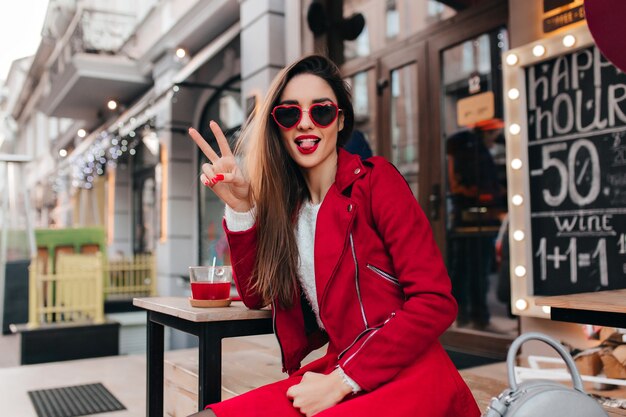 Fascinating european girl in casual red outfit having fun in cafe