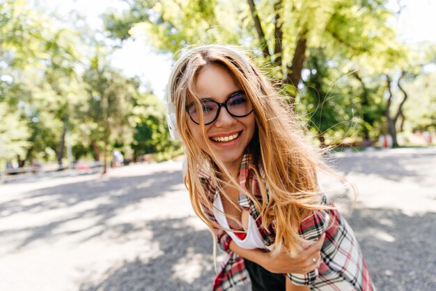 Очаровательная девушка с длинными волосами, проводящая время в парке. Модная кавказская дама смеется во время открытого лета.