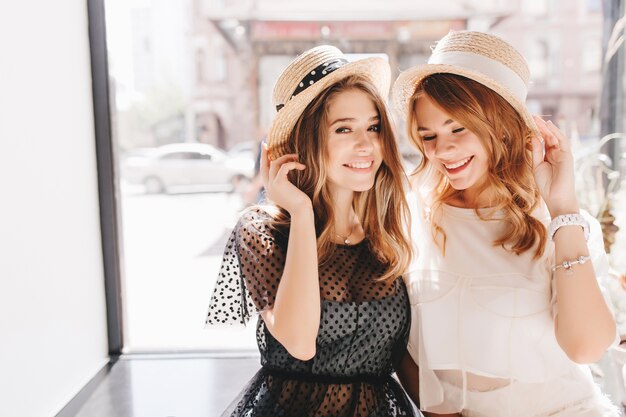 Очаровательные улыбающиеся девушки в романтических летних нарядах шутят, проводя выходные вместе