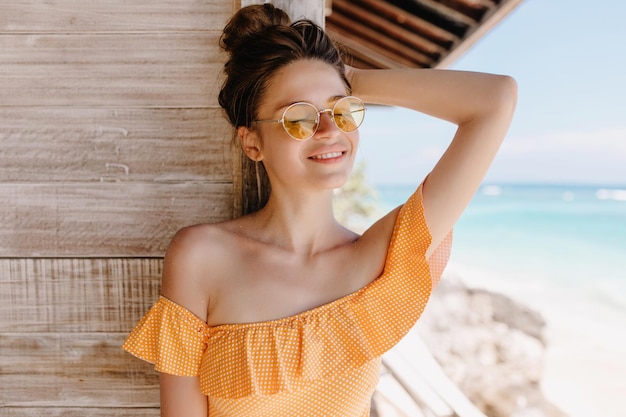 Fascinating young woman with tanned skin posing on wooden background with happy smile Outdoor shot of lovable brunette girl in orange clothes having fun at resort
