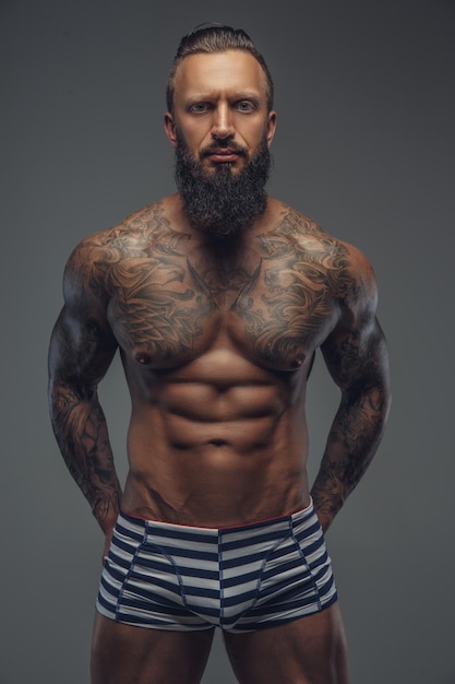 Free photo fashinable mude tattooed man with beard posing over grey background.