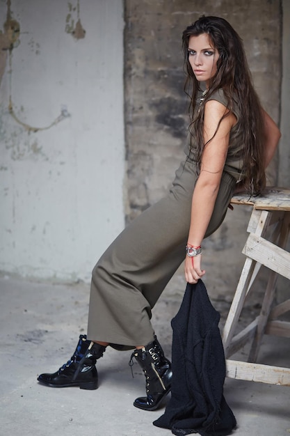 Fashinable woman in long green dress and black boots holding jacket in one hand.