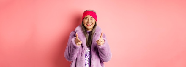 無料写真 ファッションとショッピングのコンセプト スタイリッシュな偽の毛皮のコートで ca で指を指しているクールなアジアの年配の女性