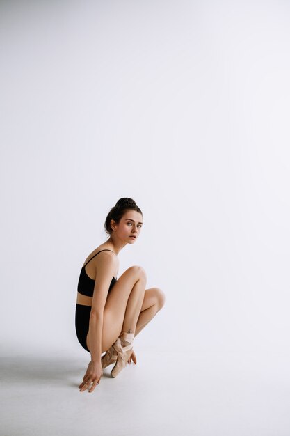 Бесплатное фото Модный балет. молодой женский артист балета в черном боди на фоне белой студии. кавказская балерина похожа на фотомодель. стиль, концепция современной хореографии. творческое художественное фото.