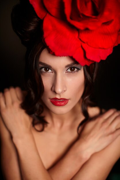 頭の上の大きな赤いバラと明るい化粧と赤い唇と美しい女性をファッションします。