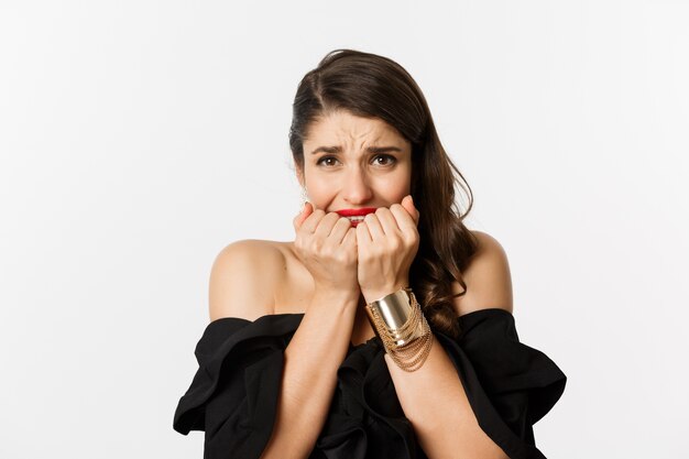 Fashion and beauty concept. Nervous woman looking concerned, biting fingernails and standing over white background.