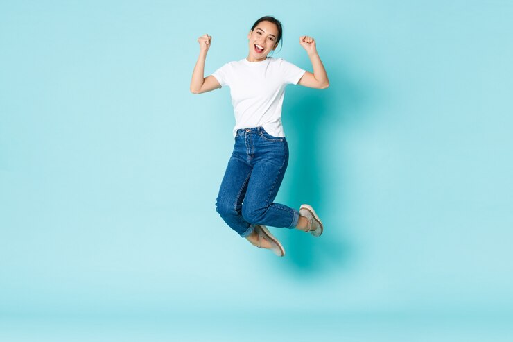 無料Photo ファッション、美容、ライフスタイルのコンセプトです。陽気な勝利、幸せと喜びからジャンプ、魅力的なアジアの女の子、水色の壁を越えて勝利を祝って、競争に勝つ