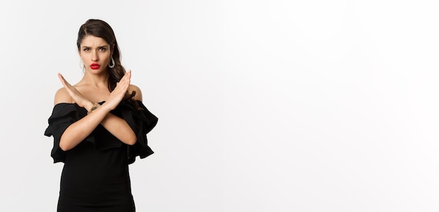 Fashion and beauty serious and confident female model in black dress showing cross sign and frowning