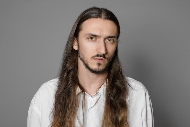 Fashion, beauty and style concept. Head and shoulders of serious bearded man with pale skin and hairy face wearing his long brown hair loose