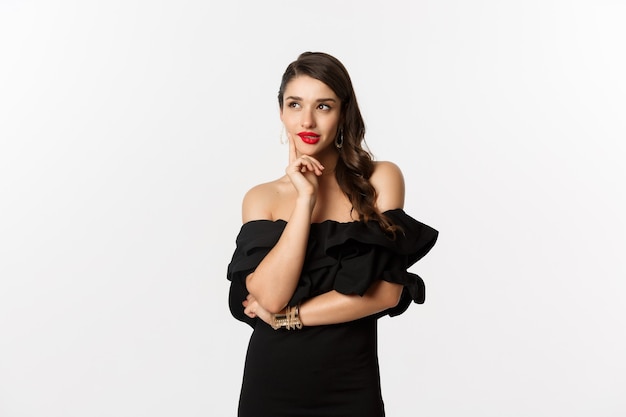 Fashion and beauty. Thoughtful young woman in black dress, smiling pleased and thinking, having an idea, white background