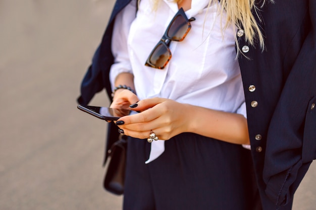 Fashion close up details of woman holding her smartphone and tap massage, official business suit and luxury trendy accessories, focus on hands.