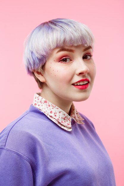 Fashion close-up portrait of smiling beautiful dollish girl with short light violet hair wearing lilac sweater over pink wall