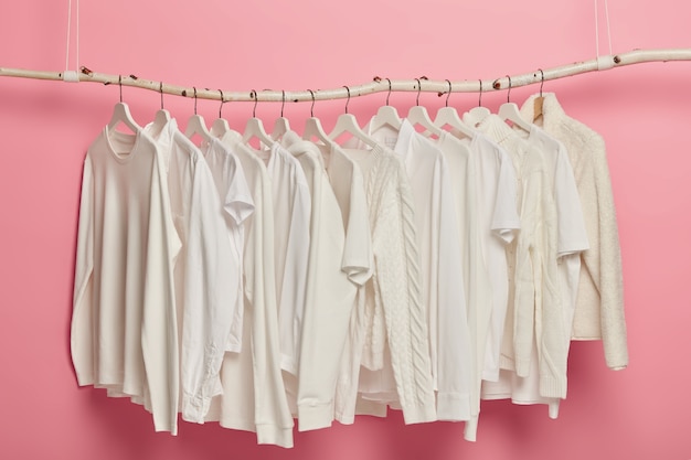 Fashion clothing of white color, knitted patterns, hanging on racks for display. Row of solid outfits in wardrobe.