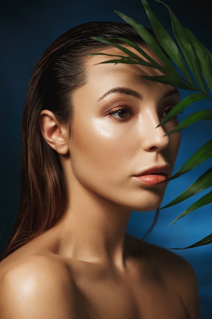 Fashion concept. Closeup of amazing woman on dark blue wall with leaves