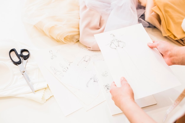 Fashion designer holding sketches in hand with many fabrics on table
