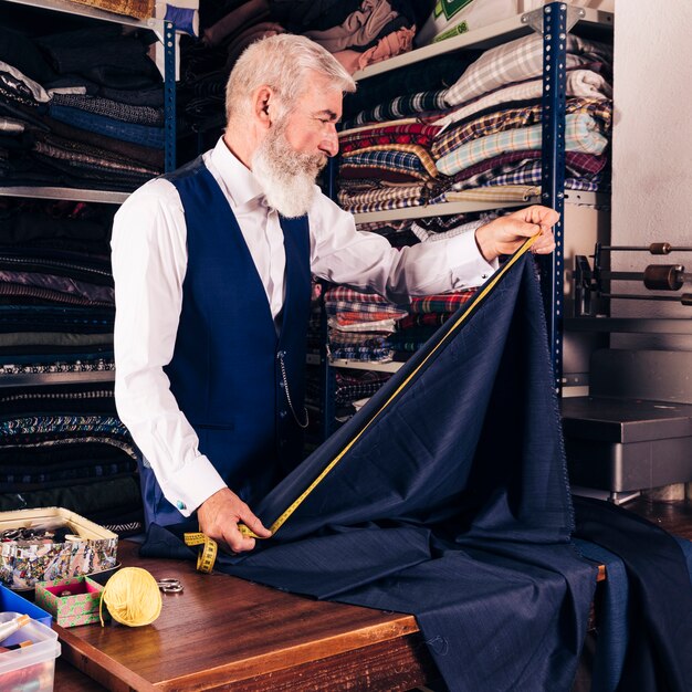 Модный дизайнер измерения голубой ткани с рулеткой на столе