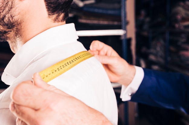 Fashion designer taking measurement of his customer's back with yellow measuring tape