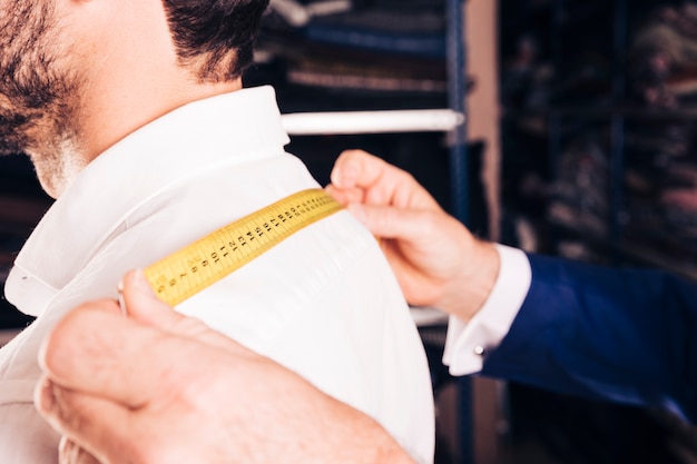 Модный дизайнер измеряет спину своего клиента желтой измерительной лентой