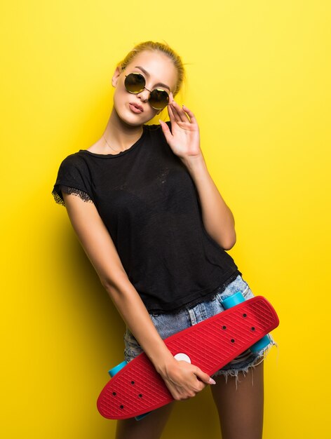선글라스와 스케이트 보드가 오렌지 배경에 대해 야외에서 재미와 화려한 옷 패션 행복 미소 hipster 멋진 여자