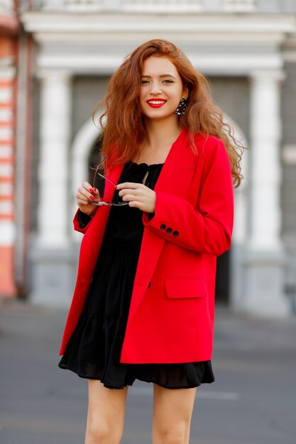 fashion model demonstrate trendy wear and accessories. Casual red jacket, black short dress.