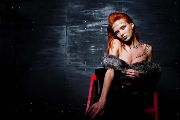 Fashion model red haired girl with originally make up like leopard predator against steel wall Studio portrait on ladder