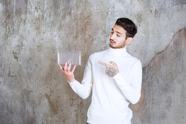 Fashion model in white sweater holding a silver gift box.