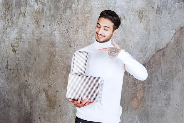 Fashion model in white sweater holding two silver gift boxes.