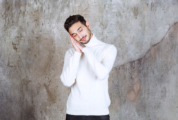 Fashion model in white sweater standing on concrete wall and looks sleepy or tired.