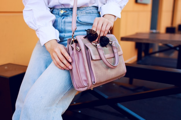 Free photo fashion objects. womanãâ¢ãâãâs hands with bag and sunglasses. fashionable girl sitting outdoor . stylish jeans.