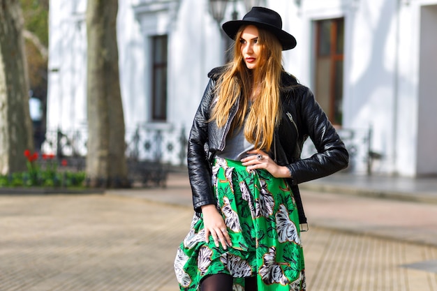 Fashion outdoor city portrait of stylish hipster woman walking on the street and having fun, young traveler woman, fashionista, feminine beauty outfit, long vintage skirt, retro hat and biker jacket.