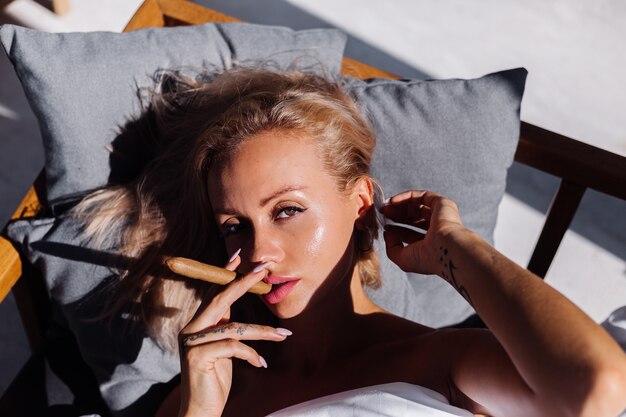 Fashion outdoor portrait of naked woman sits on sofa covering herself with blanket holding cigar