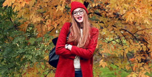 Fashion photo of blond woman with long hairs walking in sunny autumn park in trendy casual outfit.