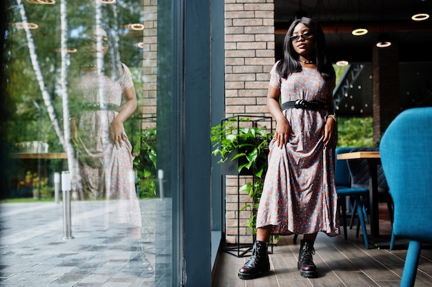 Fashion portrait of african american woman in long dress boots and sunglasses indoor