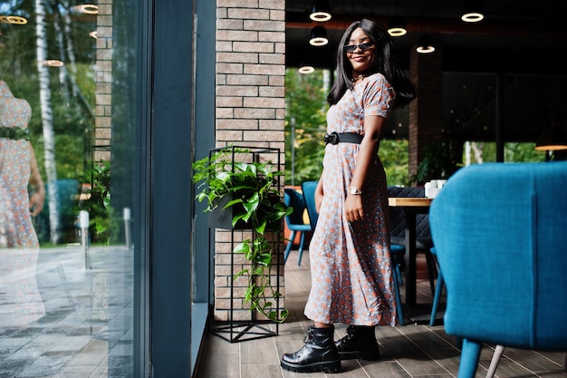 Fashion portrait of african american woman in long dress boots and sunglasses indoor