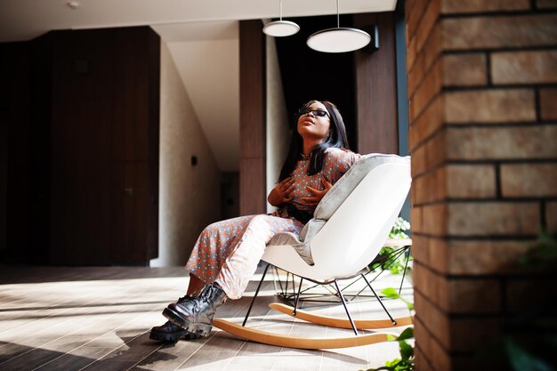 Fashion portrait of african american woman in long dress boots and sunglasses indoor